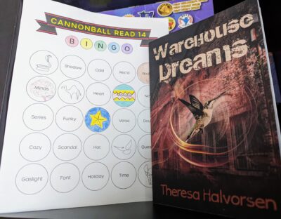 The book "Warehouse Dreams" by Theresa Halverson standing next to a book bingo card.