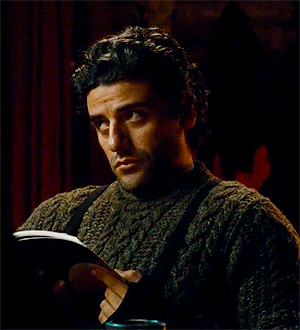 Gif of Oscar Issac reading a book, looking up, and the back down at his book.