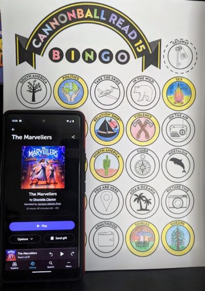 A phone displaying the audio book, "The Marvellers" by Dhonielle Clayton is standing next to a partially complete book bingo card.