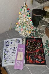 Picture of the two books Emily Wilde's Encyclopaedia of Faeries and A Strange and Stubborn Endurance sitting in front of a small porcelain Christmas tree with a bookmark