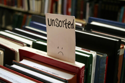 Rows of books. A note that reads "unsorted" is sticking out of one volume.
