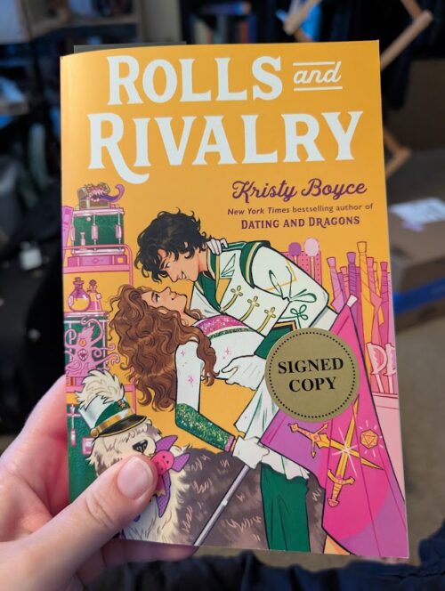 The cover of the book, "Rolls and Rivalries" by Kristy Boyce. The book has a sticker that reads Signed Edition.